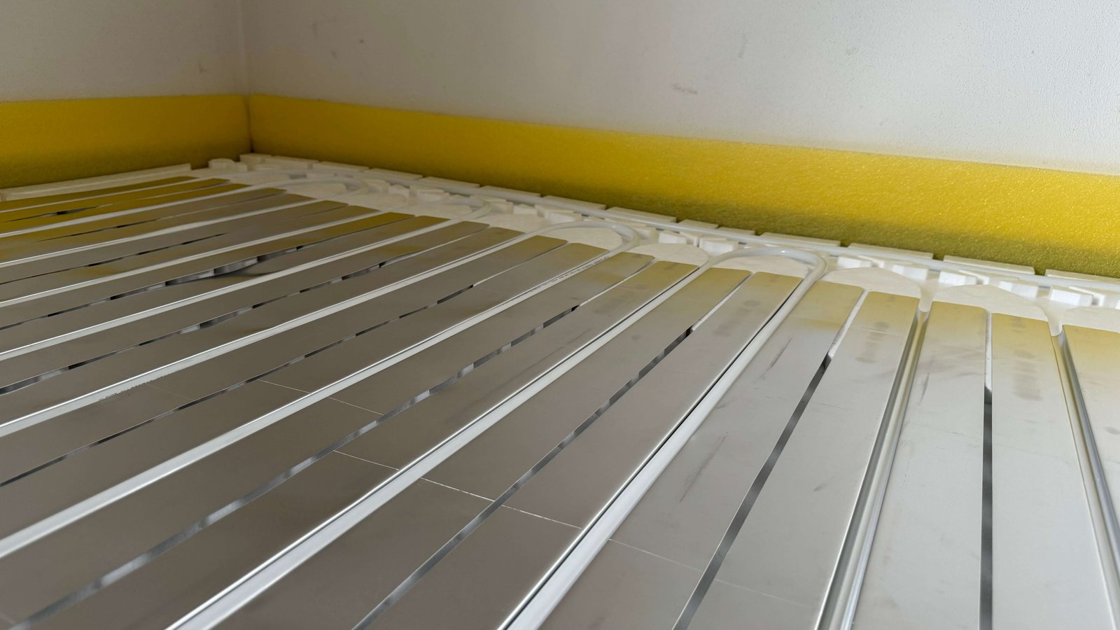 Photo of the MC Therm dry system. The heating pipe is clamped into the thermal lightweight sheet, which lies on the 25-14 EPS drywall panel. The system is bordered with a yellow edge insulation strip.