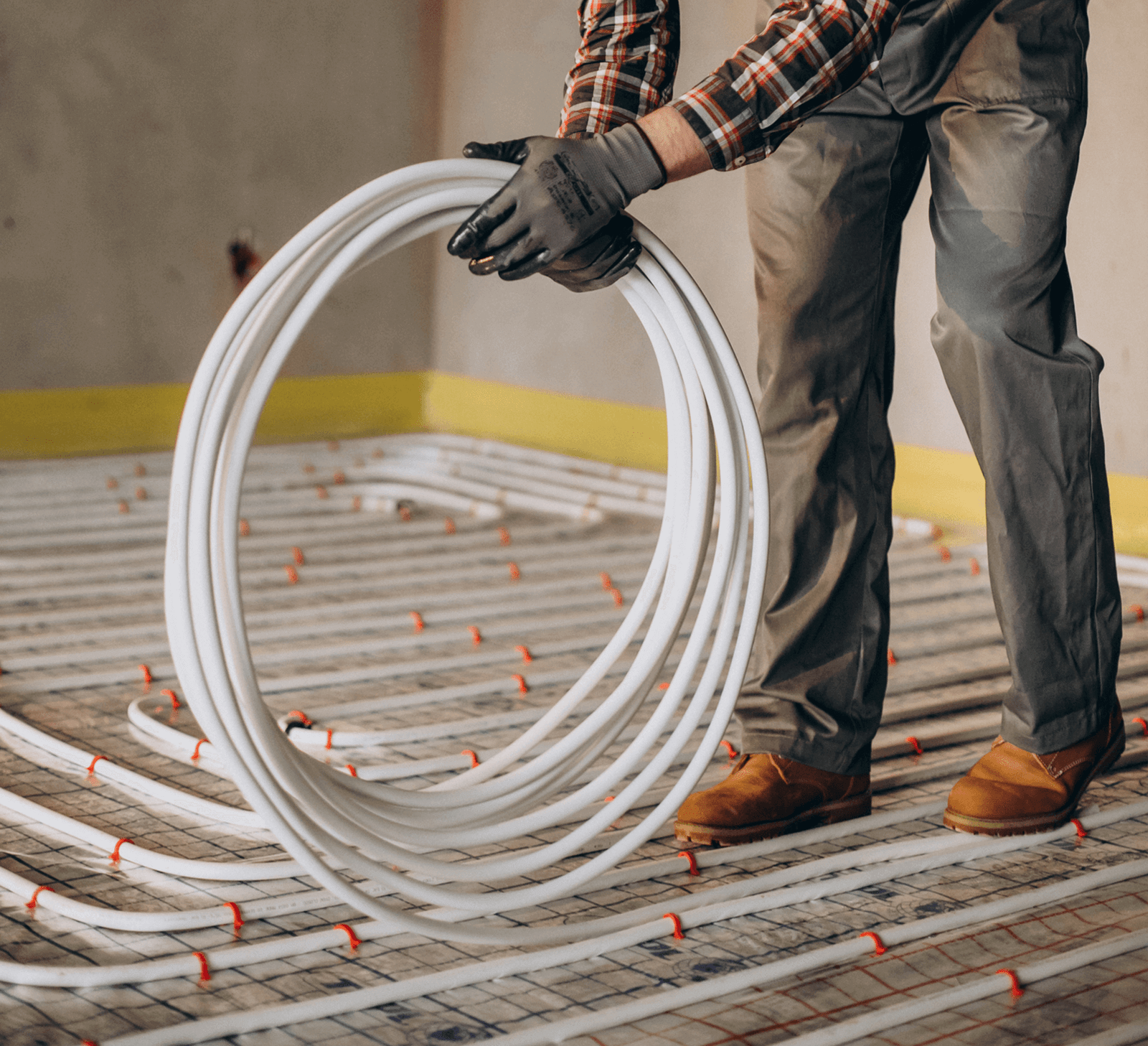 A man in work clothing is laying the heating pipe on the fabric foil. The heating pipe is secured with staples.