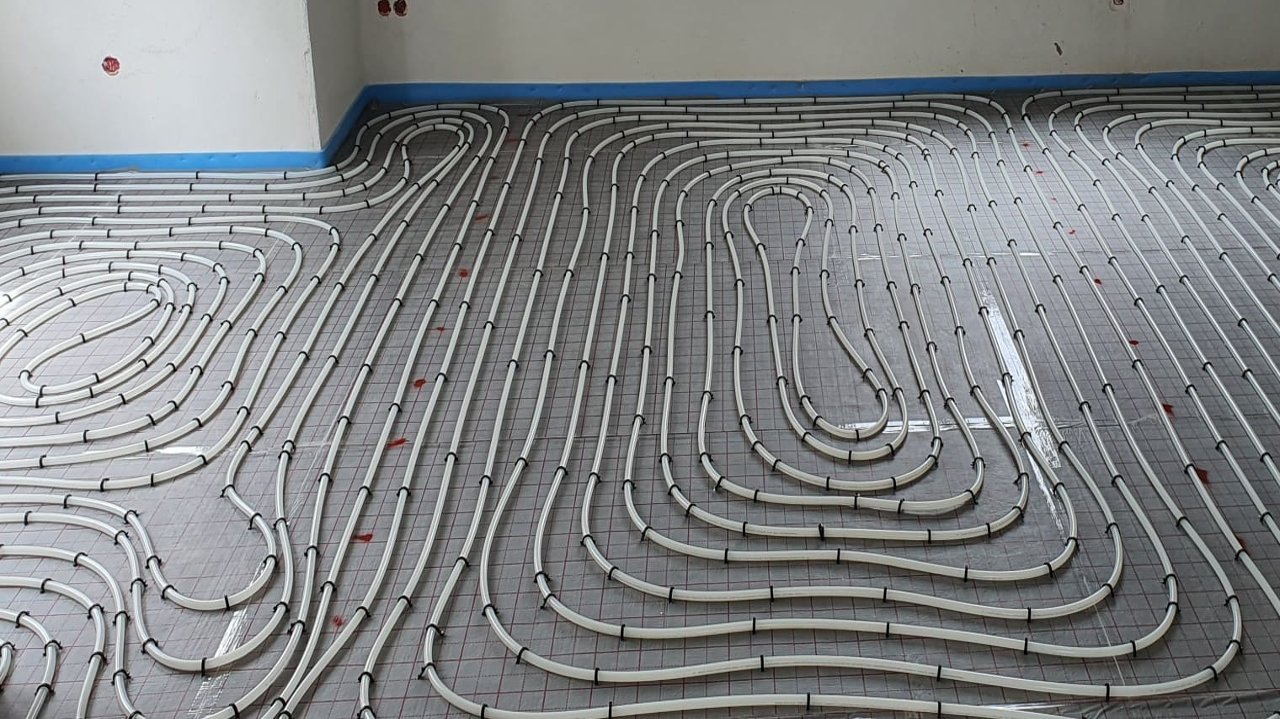 Photo of the stapling system in landscape format. The pipes are secured to the fabric foil with staples and laid in spirals. The system is bordered with a blue edge insulation strip.